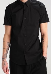 Camicia nera a maniche corte con bottoni, realizzata in tessuto liscio, con colletto classico, bottoni frontali e vestibilità su misura.