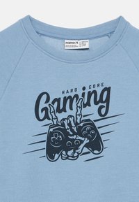 Jasnoniebieska bluza z okrągłym dekoltem z czarną grafiką przedstawiającą rękę trzymającą kontroler do gier oraz napisem "HARD CORE Gaming".