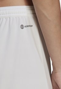 Białe sportowe szorty o gładkiej, lekkiej teksturze; posiadają elastyczną talię oraz czarne logo "AEROREADY".