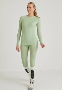 Jasnozielona warstwa bazowa z długim rękawem o dopasowanym kroju, zestawiona z pasującymi legginsami. Tkanina o fakturze z subtelnymi wzorami.