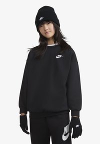 Sweatshirt Nike noir avec logo blanc, bonnet noir et gants noirs ; coupe ample, texture douce, poignets et taille côtelés.
