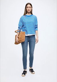 Modro-bielo pruhovaná mikina, modré džínsy, hnedá taška cez rameno, čierne tenisky s bielymi detailmi; voľný strih, ležérny dizajn.