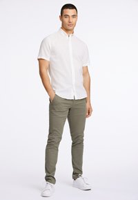 Weißes kurzärmliges Hemd mit einer schlichten Textur, kombiniert mit olivgrünen Slim-Fit-Hosen und weißen Sneakern, vor einem schlichten Hintergrund stehend.