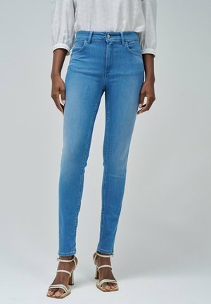 Vaqueros ajustados de tiro alto en denim de color azul claro con una textura suave, que cuentan con cierre frontal de botón y diseño de cinco bolsillos.
