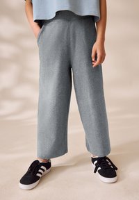 Pantaloni sportivi grigi e a gamba larga realizzati in morbido tessuto, con cintura elastica e tasche laterali, abbinati a sneaker nere con strisce bianche.