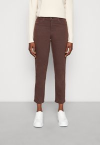 Jeans in cotone marrone elasticizzato con vestibilità slim e lunghezza cropped, dotati di cinque tasche e chiusura frontale con bottone, abbinati a sneakers bianche.