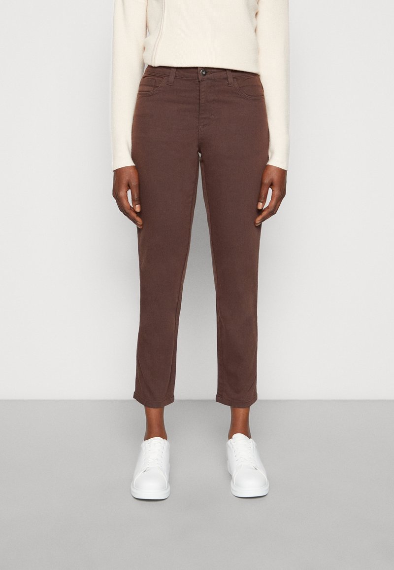 Jeans in cotone marrone elasticizzato con vestibilità slim e lunghezza cropped, dotati di cinque tasche e chiusura frontale con bottone, abbinati a sneakers bianche.