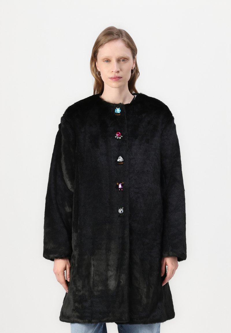 Črna umetna krznena plašč s krožnim izrezom, ki ima spredaj šest pisanih gumbov, podobnih dragim kamnom, in dolge rokave. Mehka tekstura.