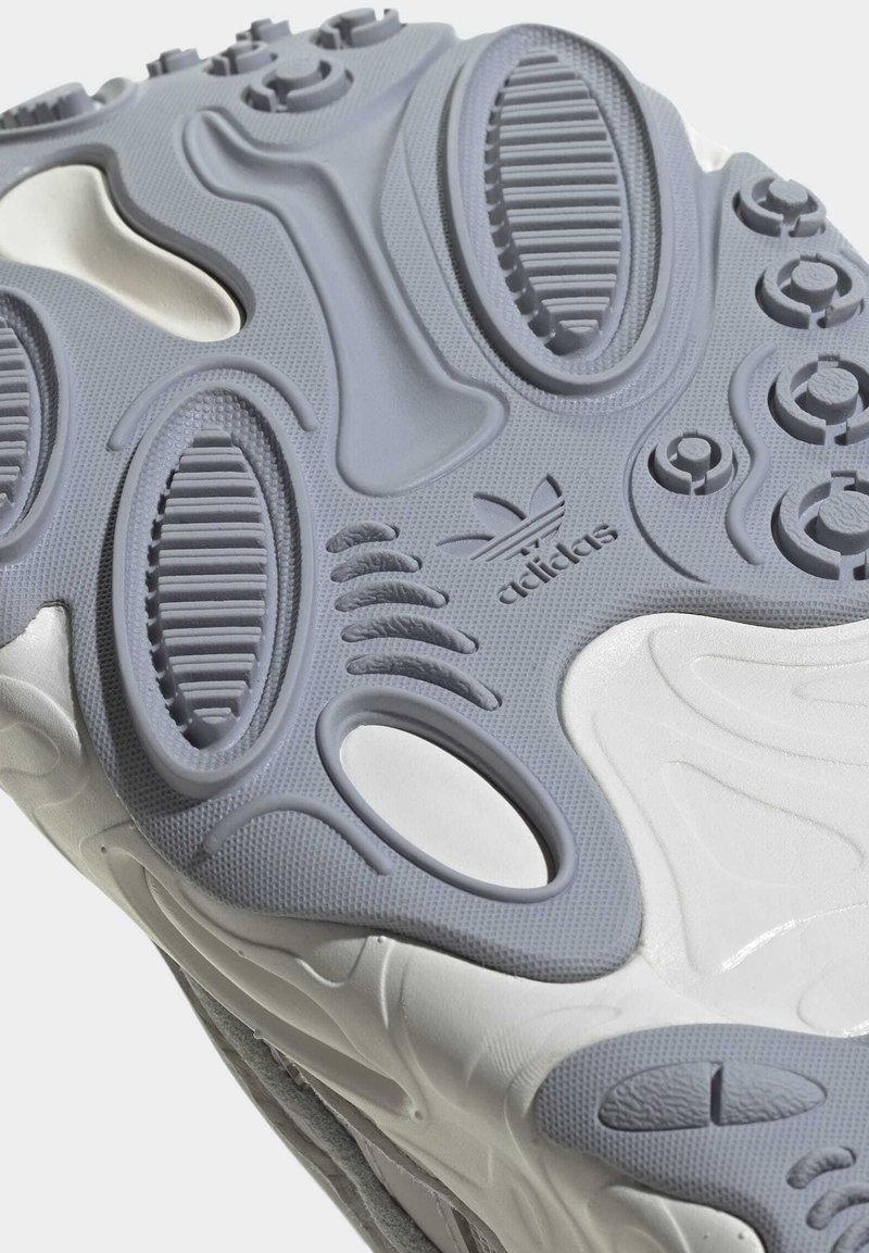 Graue Gummisohle mit strukturierten Mustern und Rillen. Das auffällige Adidas-Logo ist in das Design eingeprägt.