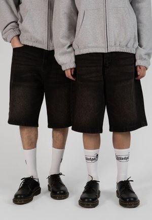 Black denim shorts with a relaxed fit, gray zip-up hoodie, black lace-up shoes, and white socks featuring text. Simple, casual ensemble.