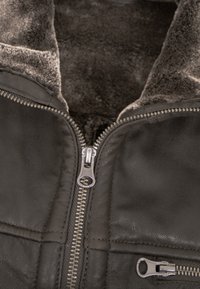 Dunkle Lederjacke mit kontrastierendem weichem Futter, ausgestattet mit einem zentralen silbernen Reißverschluss und zusätzlichen Reißverschlusstaschen.