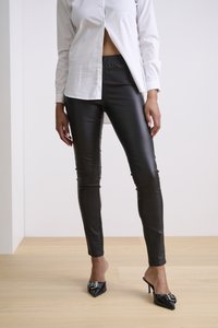 Schwarze Kunstlederhose mit taillierter Passform und elastischem Bund, kombiniert mit einem weißen Hemd und glänzenden schwarzen High-Heel-Mules.