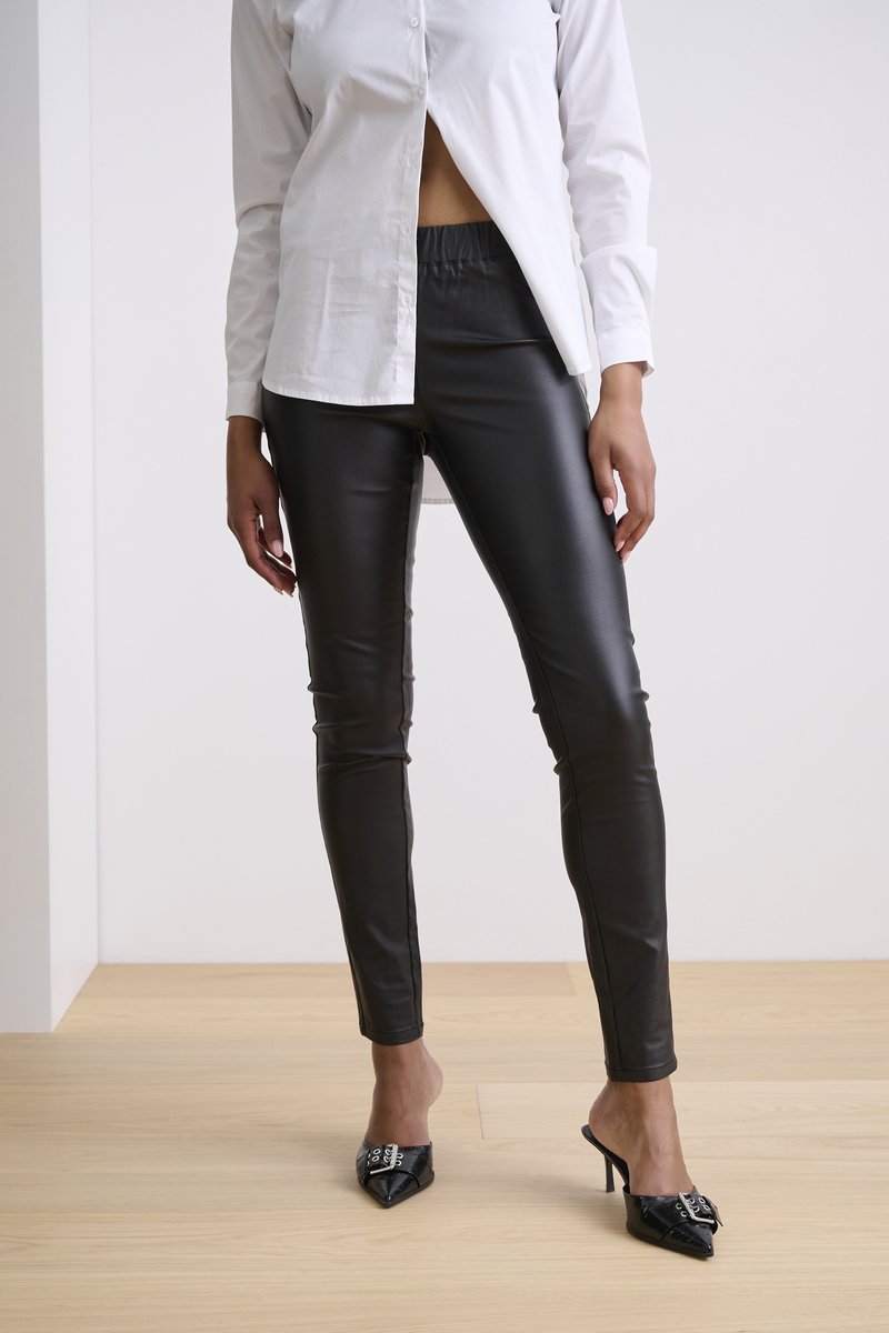 Schwarze Kunstlederhose mit taillierter Passform und elastischem Bund, kombiniert mit einem weißen Hemd und glänzenden schwarzen High-Heel-Mules.
