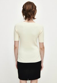 Top de manga corta acanalado color crema con escote redondo, combinado con una falda lápiz negra. Textura suave y silueta ajustada.