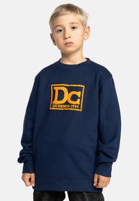 Marineblauwe sweater met een oranje DC-logo, geribbelde ronde hals en manchetten. Casual ontwerp, oversized pasvorm, gemaakt van zacht katoen.