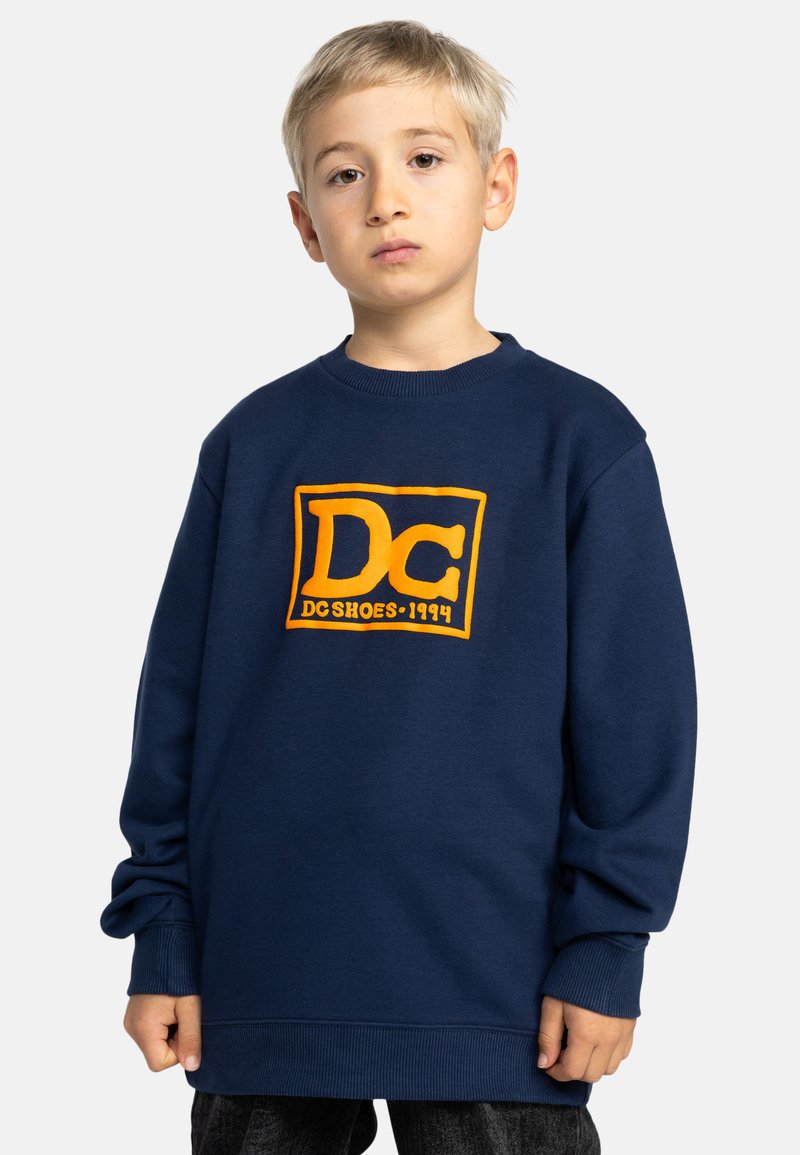 Marineblauwe sweater met een oranje DC-logo, geribbelde ronde hals en manchetten. Casual ontwerp, oversized pasvorm, gemaakt van zacht katoen.
