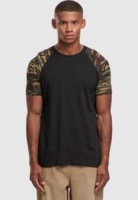 Black t-shirt with camo-patterned sleeves, featuring a round neckline and short raglan sleeves. Cotton fabric with a smooth texture.