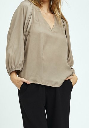 Beige Seidenbluse mit V-Ausschnitt, langen Puffärmeln und elastischen Bündchen. Kombination mit schwarzen Hosen, der Stoff hat eine glatte, glänzende Textur.