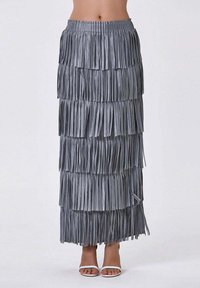 Jupe maxi gris à franges avec des franges superposées, taille élastique et une coupe fluide. Portée avec des sandales blanches simples.