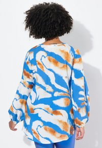 Camicia blu e bianca con maniche lunghe fluide, caratterizzata da un motivo astratto ondulato marrone e bianco. Collo arrotondato, tessuto leggero.