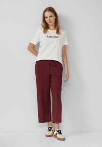 Witte T-shirt met de tekst "Amour", gecombineerd met bordeaux brede broek en beige sneakers met zwarte veters en accenten.