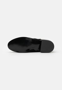 Suela de zapato negra con un acabado suave y brillante, con sutiles surcos para agarre. Forma plana y redondeada con un ligero tacón para estabilidad.