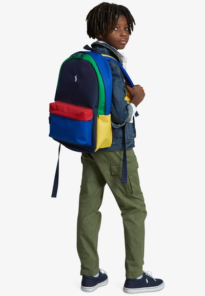 Mochila colorida con secciones en navy, verde, amarillo y rojo, hecha de un tejido durable; cuenta con correas acolchadas y un bolsillo frontal.