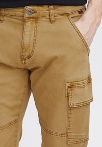 Spodnie cargo w kolorze khaki, wykonane z miękkiej mieszanki bawełny, z wieloma kieszeniami, przeszyciami oraz zapięciem na guzik w talii.