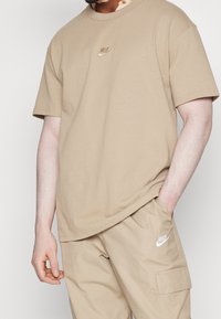 Beige bavlněné tričko s malým tónovým logem Nike na hrudi. Krátké rukávy a uvolněný střih, doplněné o odpovídající béžové kalhoty.