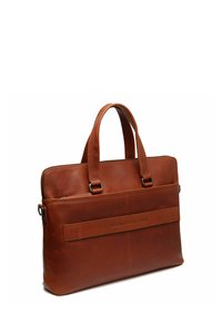 Sacoche en cuir marron pour ordinateur portable avec deux poignées supérieures, fermeture zippée et poche avant arborant un logo en relief. Texture lisse et forme rectangulaire.