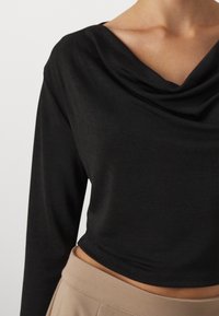 Schwarzes Langarmtop mit drapierter Schalkragen. Hergestellt aus glattem Stoff, hat es einen verkürzten Schnitt und passt gut zu beigen, hoch sitzenden Hosen.