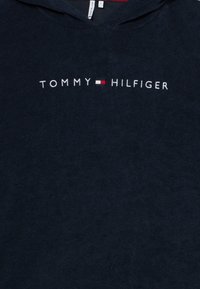 Μπλε ναυτικό φούτερ με κουκούλα από απαλό ύφασμα που παρουσιάζει το κείμενο "TOMMY HILFIGER" σε λευκό με κόκκινες και λευκές λεπτομέρειες.