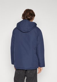 Veste rembourrée bleu marine avec capuche, présentant une texture lisse et une coupe droite. La capuche repose à plat sur la zone du col.