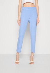 Light blue tapered pants made of soft fabric, featuring a smooth waistband, subtle seams, and a clean hemline. Paired with nude strappy heels.