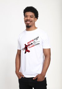 Weißes Baumwoll-T-Shirt mit einem grafischen Druck eines roten Charakters mit schwarzen Akzenten und dem Text "MARVEL STUDIOS". Standardpassform.