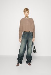 Braunes, kurzes Langarm-Henley-Shirt mit Knopfleiste; lockere, dunkelblaue Jeans; schwarze Handtasche; braune Sportschuhe.