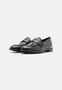 Mocasines de cuero negro con un acabado brillante, que presentan un diseño cosido, acentos de hardware dorado y un tacón bajo.