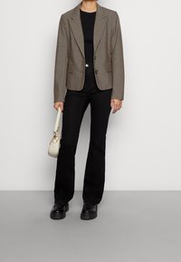 Ruskea, muotoiltu bleiseri teksturoitua kangasta, jossa on kaksi nappia ja läppätaskut, yhdistetty mustaan yläosaan ja hulmuaviin mustiin housuihin. Valkoinen käsilaukku, mustat kengät.