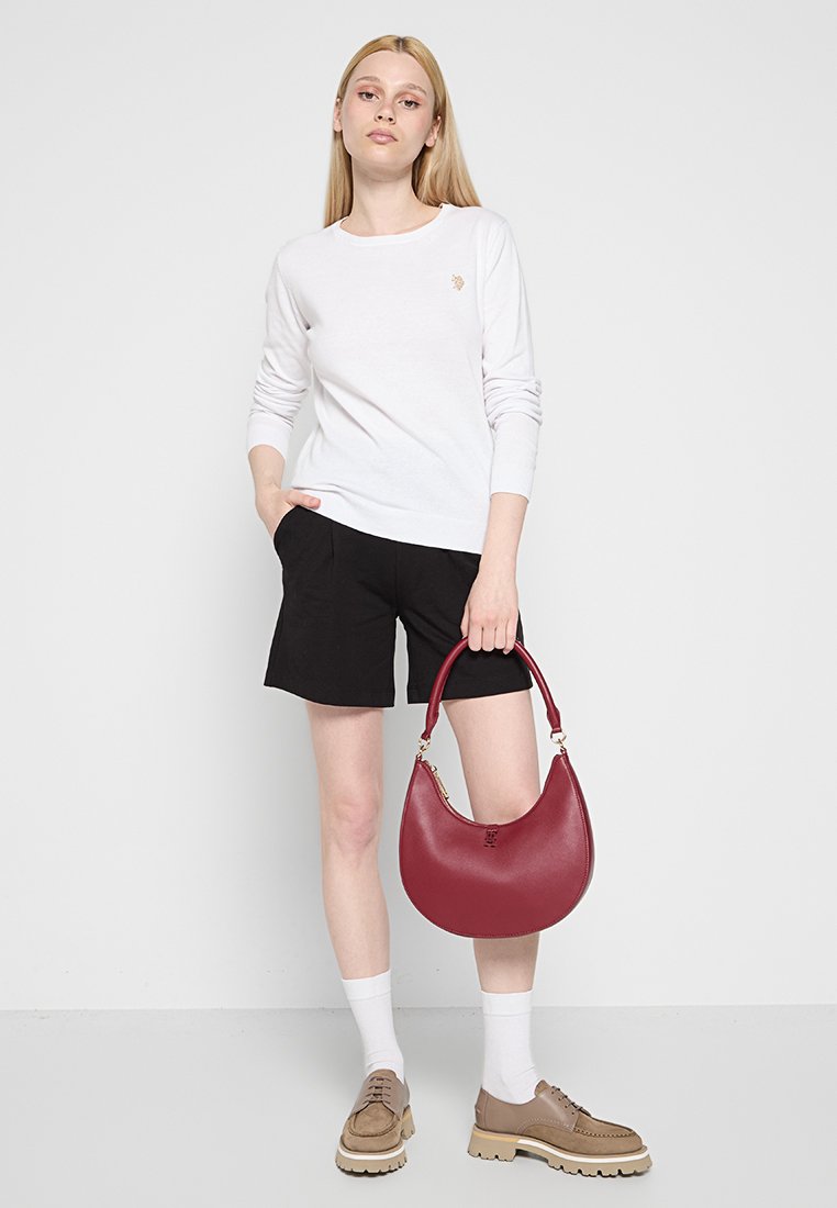 Rote Leder-Hobo-Tasche mit geschwungener Form, goldenen Beschlägen und glatter Textur. Getragen mit einem weißen Langarmshirt und schwarzen Shorts.