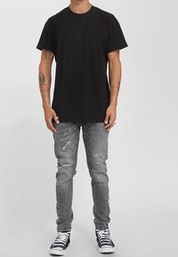 Svart bomullströja med korta ärmar, kombinerad med grå slitna jeans och svartvita högknäbågs-sneakers. Enkla bakgrund.