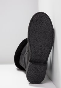 Botte noire avec une semelle en caoutchouc texturé, dotée d'une doublure en peluche à l'ouverture. Matériau supérieur lisse et design minimaliste.