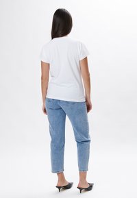 Camiseta blanca de manga corta combinada con jeans de mezclilla azul claro, con un corte recto y dobladillos doblados. Tacones negros tipo slip-on complementan el conjunto.