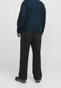 Czarne, luźne spodnie z tylną kieszenią, zestawione z ciemnoniebieskim swetrem o teksturowym splocie i czarnymi butami sportowymi.