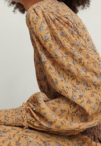 Vestido floral amarillo con tejido texturizado, con mangas abullonadas, puños elásticos y detalles fruncidos. Pequeños patrones de flores azules y blancas.