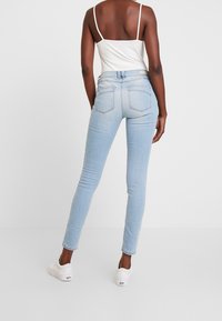 Jeans ajustados de color azul claro en denim suave. Con un talle alto, bolsillos traseros y un ligero desgaste. Combinados con zapatillas blancas.