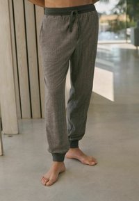 Graue Fischgräten-Jogginghosen mit einem dunkelgrauen elastischen Bund und Bündchen. Verfügt über Seitentaschen und einen Kordelzugverschluss. Ideal für die Freizeit.