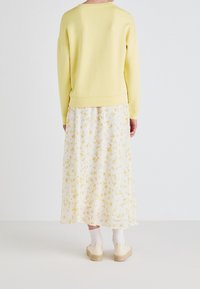 Geel sweatshirt met een ronde hals, gecombineerd met een witte rok met een geel bloemenpatroon. De outfit wordt compleet gemaakt met beige platform schoenen.