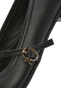 Zapato de cuero negro con punta redondeada, textura suave y un acento metálico en tono dorado con un detalle de lazo en la correa.