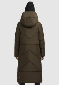 Dlhý, olivovo zelený puferový kabát s kapucňou, s chevronovým prešívaním a malou logovou nálepkou pri spodnom leme. Pletená čierna čiapka.