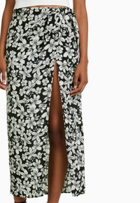 Černá maxi sukně s květinovým potiskem a bílými květy, s bočním rozparkem a vázáním v pase, vyrobená z lehkého materiálu.